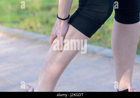 Jeune femme jogger souffrant de crampes ou spasmes des muscles du mollet en se penchant à l'embrayage sa jambe dans sa main tandis qu'elle court le long d'un chemin par les fi Banque D'Images