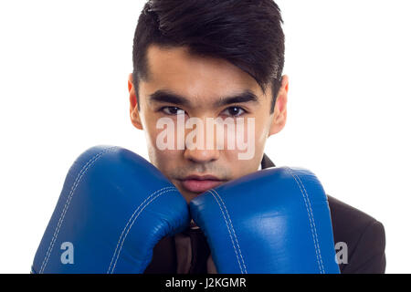 Jeune homme séduisant avec des cheveux noirs en chemise blanche et cravate avec smoking noire et des gants de boxe bleus sur fond blanc Banque D'Images