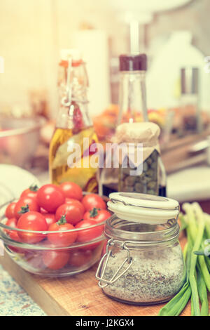 Avec sel, épices caper dans un bocal en verre, le vinaigre balsamique et l'huile d'olive avec du poivre et épices dans des bouteilles en verre, matières premières tomates cerises fraîches dans bol en verre Banque D'Images