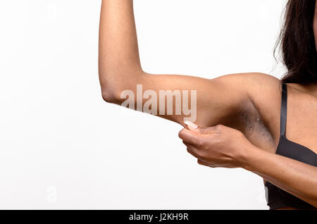 Jeune femme africaine afficher la peau lâche ou flab due au vieillissement sur son bras la pinçant entre ses doigts, vue en gros Banque D'Images