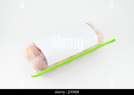Oeufs dans le coffret en plastique avec du ruban adhésif vert sur fond blanc Banque D'Images