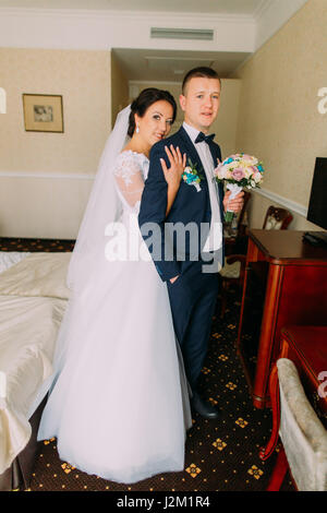 Mariée magnifique et élégant groom posing dans chambre d'hôtel après la cérémonie du mariage. Portrait de jeunes mariés en lune de miel Banque D'Images