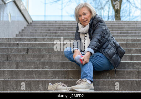 Senior femme sans défense en massant son pied à revivre et courbatures après tomber comme suit Banque D'Images