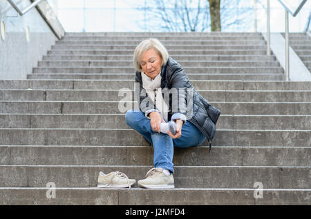 Senior femme sans défense en massant son pied à revivre et courbatures après tomber comme suit Banque D'Images