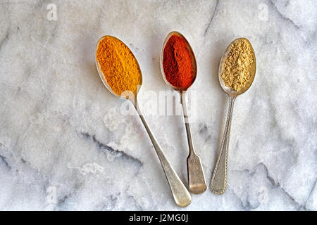 Passage de trois cuillères en métal avec le curcuma, le paprika et le gingembre spice sur un arrière-plan en marbre blanc Banque D'Images