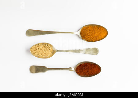 Passage de trois cuillères en métal avec le curcuma, le paprika et le gingembre spice sur un arrière-plan uni, blanc Banque D'Images