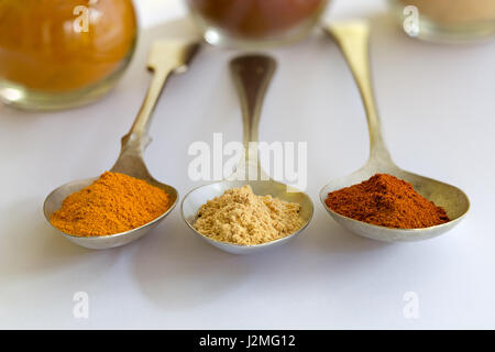 Trois cuillères en métal avec le curcuma, le gingembre et le paprika, épices sur un arrière-plan uni, blanc, en pointant sur l'appareil photo avec soft-focus bols à l'arrière. Banque D'Images