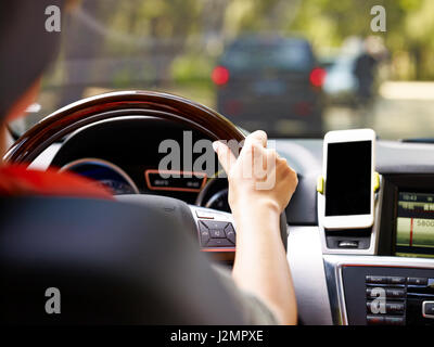 Main d'une femme tenant le volant d'un véhicule équipé d'un téléphone cellulaire sur le tableau de bord. Banque D'Images