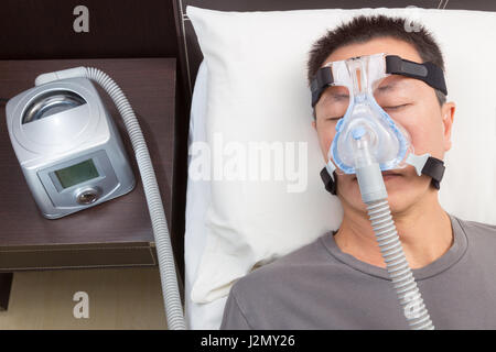 L'homme asiatique avec l'apnée du sommeil à l'aide d'appareil CPAP, le port de masque harnais connexion au tube d'air, selective focus sur le masque et le harnais de l'homme Banque D'Images