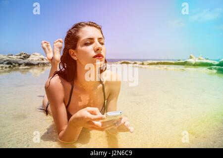 Femme portant sur la plage avec téléphone Banque D'Images