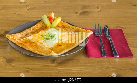 Crêpe délicieuse avec le fromage cheddar et les cornichons à côté servi sur une plaque gris sur une table en bois avec fourchette et couteau sur une serviette rouge Banque D'Images