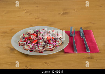 Assiette de gaufres belges de fruits mélangés avec du chocolat et sauce aux fraises servi avec fourchette et couteau sur serviette rouge. Banque D'Images