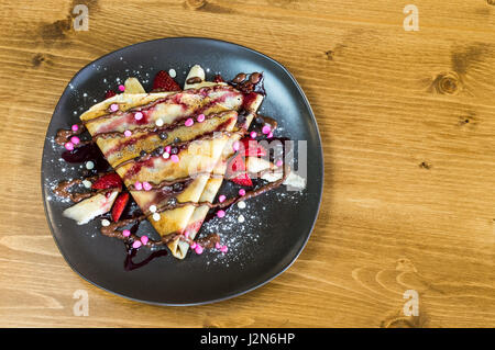Vue de dessus de la crêpe avec crème au chocolat, chocolat, fraise et banane servi sur plaque gris sur une table en bois Banque D'Images