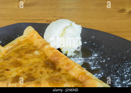 Gros plan du crêpe délicieuse avec du miel et de la crème glacée servie sur une plaque gris sur une table en bois Banque D'Images