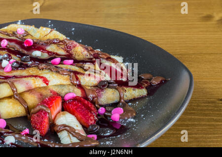 Libre de la crêpe avec crème au chocolat, chocolat, fraise et banane servi sur plaque gris sur une table en bois Banque D'Images