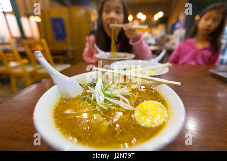 Bols de nouilles ramen avec arrière-plan flou de l'asian kid manger et un autre enfant à regarder, selective focus sur l'oignon vert et blanc Banque D'Images