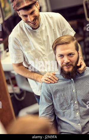 Habile coiffure coupe de cheveux faisant sourire barbu trop client à barbershop Banque D'Images