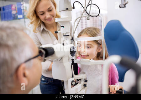 Mère et fille parler avec spécialiste des yeux quand il regarder l'objectif dans l'oeil de l'enfant avec l'ophthalmoscope Banque D'Images