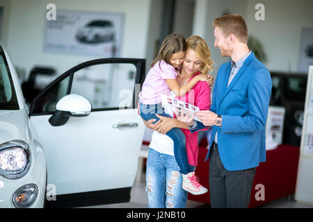 Jeune femme avec enfant en voiture à la recherche de brochure avec vendeur Banque D'Images