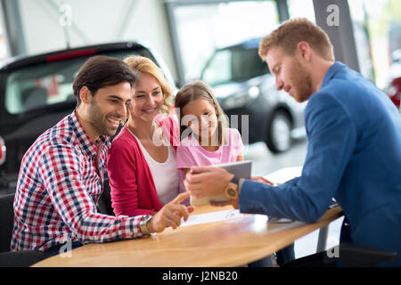 Famille heureuse dans l'agence de voiture le choix de leur nouvelle voiture, voiture sympa d'aider l'agent Banque D'Images