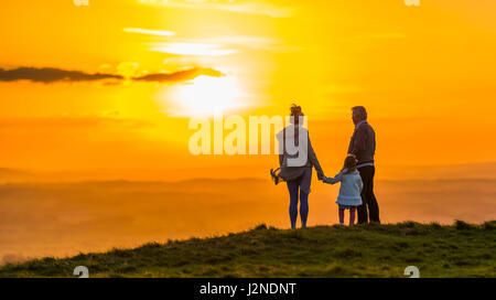 Petite famille debout sur une colline regardant le coucher du soleil tout en se tenant la main. Concept d'être ensemble. Concept toujours. Concept de proximité. Banque D'Images