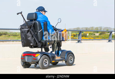 Un homme âgé sur un chemin dans un scooter de mobilité électrique pour les personnes à mobilité réduite. Banque D'Images