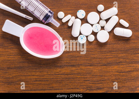 Tas de pilules blanches, thermomètre numérique, seringue, et médicament liquide en cuillère en plastique, le tout sur la table en bois Banque D'Images