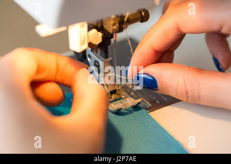 De couture et de quilting à la main dans l'atelier d'un tailleur : gros plan sur les doigts de la femme sur mesure avec manucure stick bleu machine à coudre aiguille fil Banque D'Images