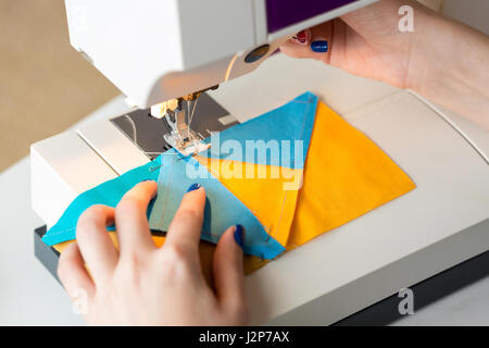 De couture et de quilt à l'atelier d'un tailleur : gros plan sur les mains d'une femme travaillant sur machine à coudre sur mesure cousu avec des morceaux de tissu bleu et jaune Banque D'Images