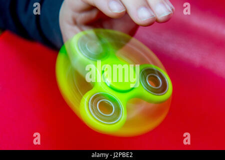 Dimanche 30 Avril 2014 Photo : vert vif fidget spinner en utilisation sur un fond rouge Banque D'Images