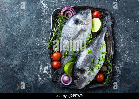 Poisson cru frais Dorado ou dorade avec des ingrédients pour la cuisine sur fond sombre, vue du dessus Banque D'Images