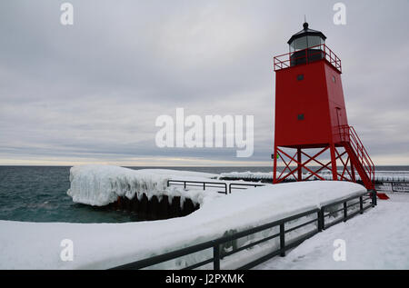 Un phare rouge se trouve à l'extrémité d'un quai couvert de neige et de glace sur un jour nuageux. Banque D'Images