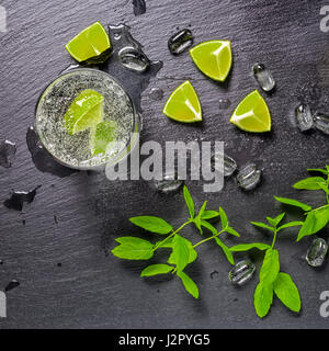 Mojito cocktail avec splash, glace, menthe verte, essence limes et gouttes sur fond d'ardoise noire, Close up Banque D'Images