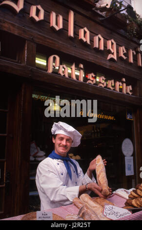 BOULANGERIE BAGUETTE PÂTISSERIE BAKER PÂTISSERIE FRANCE casquette française posant avec baguette fraîchement cuite, à l'extérieur avec son marché du pain, stand Honfleur France Banque D'Images