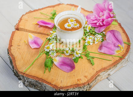 Tasse de thé sur un disque de bois de bouleau, décoré de feuilles et fleurs tulipes chomomile Banque D'Images