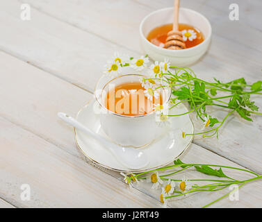 Bol rempli avec du miel de fleurs et la cuillère avec une tasse de thé, décorée avec la camomille Banque D'Images