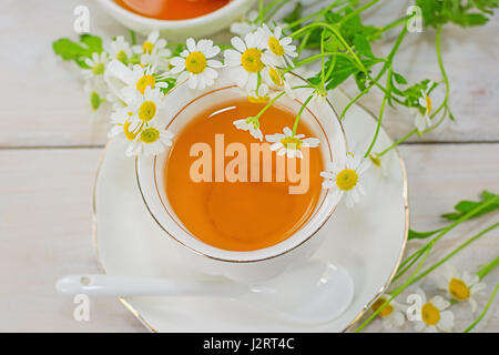 Bol rempli avec du miel de fleurs et la cuillère avec une tasse de thé, décorée avec la camomille Banque D'Images