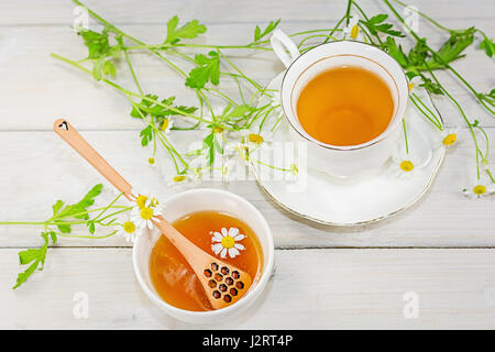 Bol rempli avec du miel de fleurs et la cuillère avec une tasse de thé, décorée avec la camomille Banque D'Images