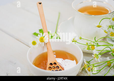 Bol rempli avec du miel de fleurs et la cuillère avec une tasse de thé, décorée avec la camomille Banque D'Images