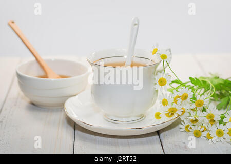 Bol rempli avec du miel de fleurs et la cuillère avec une tasse de thé, décorée avec la camomille Banque D'Images