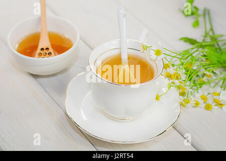 Bol rempli avec du miel de fleurs et la cuillère avec une tasse de thé, décorée avec la camomille Banque D'Images