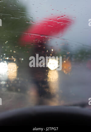 Derrière le volant - silhouette d'un homme avec parapluie rouge, photo prise de la voiture, derrière le pare-brise Banque D'Images