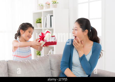 Jeune mère assise sur le canapé à la maison a reçu une surprise de sa fille se sentir excité ouvrir la bouche et à la recherche à la stupéfaction en cadeau Banque D'Images