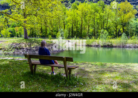 Vue arrière de la figure féminine s'assit sur le banc à la rivière au lac Banque D'Images