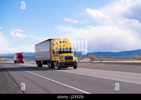 Rouge et jaune moderne gros camion camions semi remorques à venir dans un convoi, un par un et des marchandises transportées droit comme une flèche avec l'autoroute séparés Banque D'Images