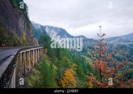 Panorama de la vallée pittoresque de Columbia River Gorge avec les arbres aux couleurs automnales et la brume sur les montagnes et semi chariot en mouvement sur un pont en béton Banque D'Images