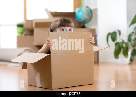 Joli enfant assis à l'intérieur d'une boîte après déménagement en appartement neuf Banque D'Images