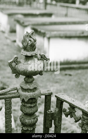 Un poteau de clôture ouvragée se trouve au-dessus d'une porte en fer forgé dans un ancien cimetière. Au-dessus du sol cryptes sont vu derrière elle. Banque D'Images