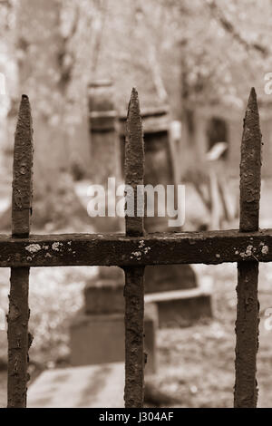 Les pierres tombales sont vus au-delà une vieille clôture de fer rouillé, dans un cimetière cimetière. L'image est fait d'une nuance de couleur sépia. Banque D'Images