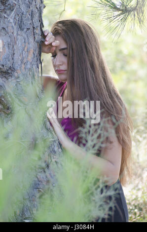 Sad young woman leaning against a tree Banque D'Images